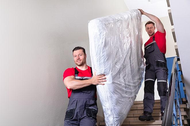 two people carrying a box spring down a staircase in Beverly Shores