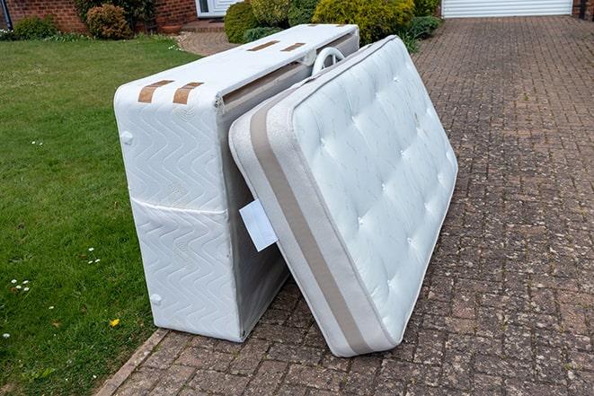 two people lifting a worn-out mattress onto a truck for removal